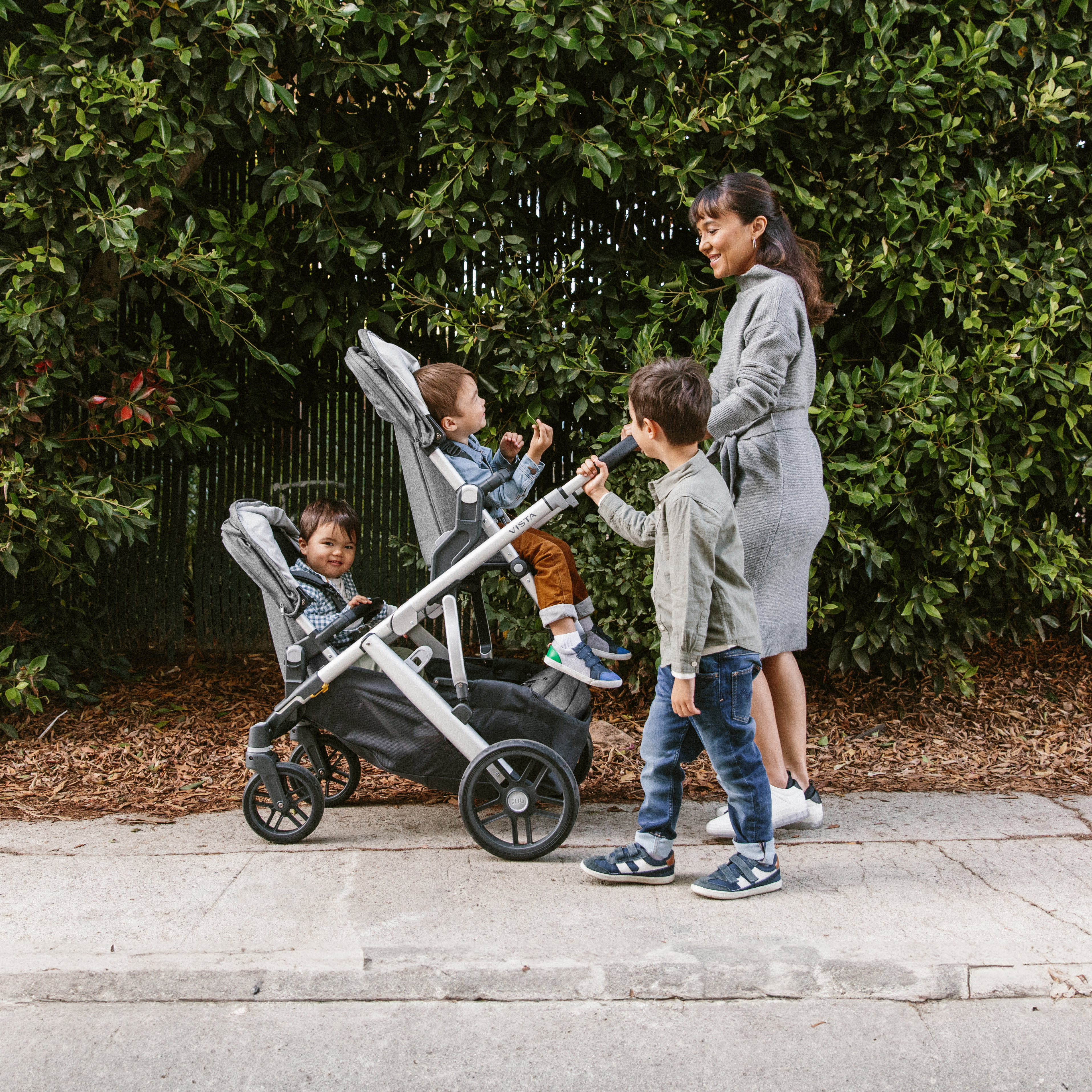 A baby in a stroller is looking up and smiling at an adult who is crouched down in front of them, engaging with the baby.
